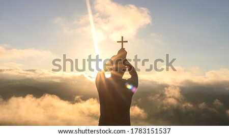 Human praying to the GOD while holding a crucifix symbol with bright sunbeam on the sky