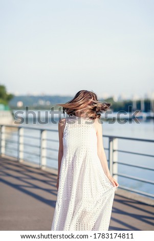 Beautiful girl whirls in a white dress on the embankment of the river