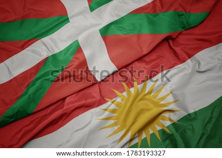 waving colorful flag of kurdistan and national flag of basque country. macro