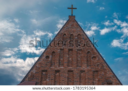Fragment of red brick Gothic style building with catholic cross on bright blue summer sky.