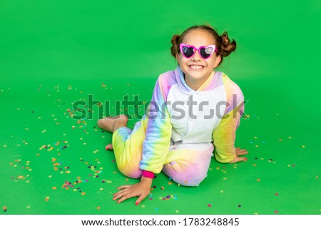 a little girl is sitting on a green isolated background with a streamer in a bright suit and glasses. Space for text. The concept of a holiday, Birthday and sales