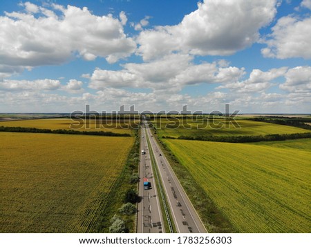 smooth road with cars that passes through yellow fields with sunflowers aerial photography