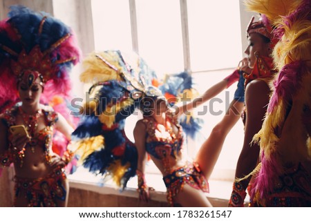 Woman in brazilian samba carnival costume with colorful feathers plumage relax in old entrance with big window.