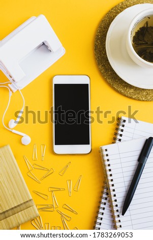 Vertical flat lay with a smartphone, cup of green tea and stationery on yellow background. Studying or working concept