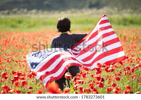 Attractive woman holding Flag of the United States in beautiful summer field on a clear, sunny day. Celebrating Independence Day, National holiday concept.
