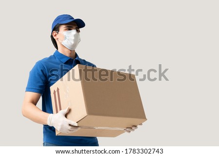 Young delivery man wearing face mask and gloves while carrying cardboard box during coronavirus outbreak Royalty-Free Stock Photo #1783302743
