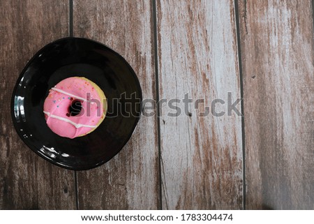 A delicious strawberry flavour donut on black dish over wooden background