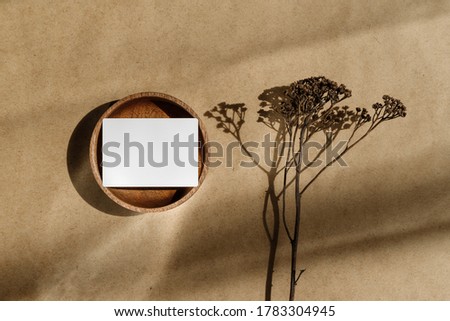 Top view of blank paper sheet card on wooden bowl with dry grass. Beige or sand tones. Mockup for business template, copy space.