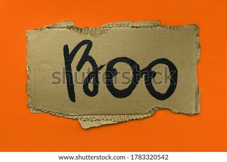 The inscription Boo in black paint on a piece of cardboard on a yellow background, the concept of the holiday Halloween