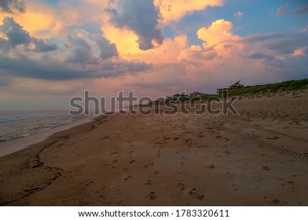 Footsteps in the sand lead down the beach in Duck North Carolina under a dramatic early morning sky.