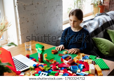 Girl playing with constructor at home, watching teacher's online tutorial on laptop. Digitalization, remote education concept. Technologies and devices. Man showing, giving online lesson. Artwork.