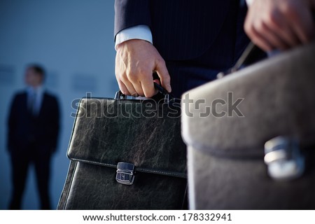 Cropped image of business partners carrying briefcases on the foreground while their colleague standing on the background  Royalty-Free Stock Photo #178332941