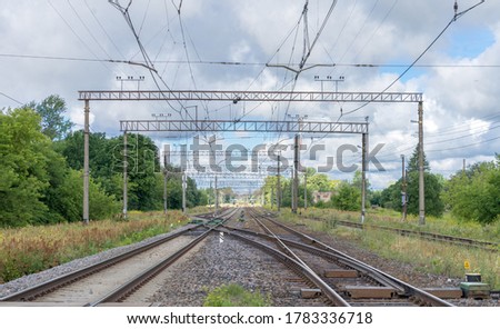 Raasiku / Estonia - July 25 2020: Steel railway lines concentrated into center in horizon. Raasiku station, towards Tallinn. Electricity lines over the scene. White clouds in bright summer morning.