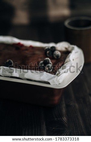 
brownie cake garnished with frozen blackcurrant berries in a brown mold with white parchment on a dark background