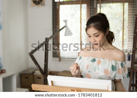 Asian woman painting oil color on a canvas. She is in her home enjoying her work