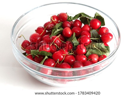 Top view of a glass bowl full of cherries and some leaves on a white background. 