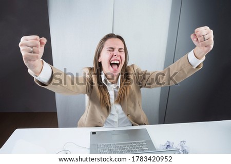 elegantly dressed blonde girl is sitting in her workplace and exults for the results achieved