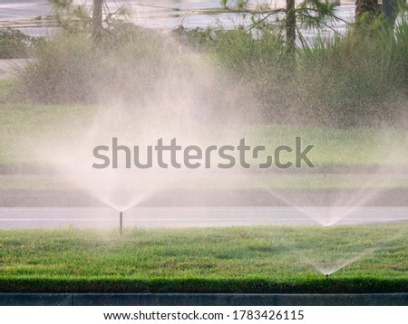 Three sprinklers watering the green median strip of a paved suburban street on a spring evening in west central Florida Royalty-Free Stock Photo #1783426115