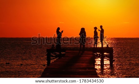 People admire and photograph the sunrise on a pier overlooking the sea in Mallorca. Only the silhouette of the people is visible in front of the red sky.
