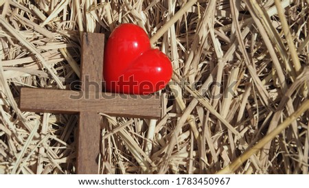 Blur Wooden holy cross and red heart on dry straw. Concept : Jesus born on manger with love. Christmas and nativity , illustration love of Christ.