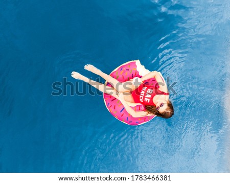 Aerial top view Young woman swimming on inflatable pink donut in transparent blue sea.