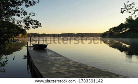 Lake at dawn, calm water, fishing boat. American countryside scenery in the early sunny morning, summertime. Midwestern nature 