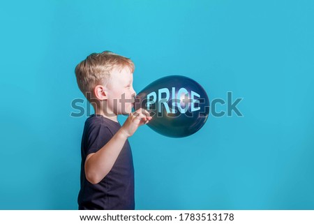 Cute boy blond European in a black t-shirt on a blue background in the Studio. A surprised beautiful funny Child inflates and bursts a balloon with the inscription price on black Friday.