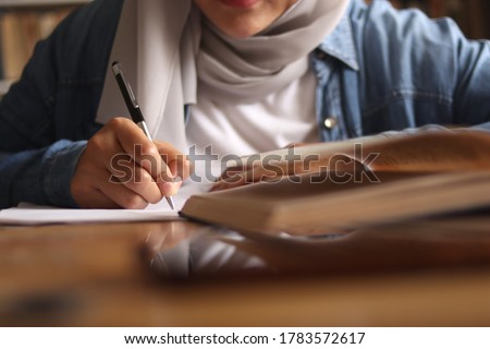 Asian muslim woman studying learning in library, exam preparation concept. Female college student doing research and making notes in her book