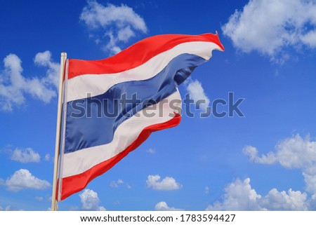 Thai flag waving in wind, with white clouds and beautiful blue sky as backdrop.
