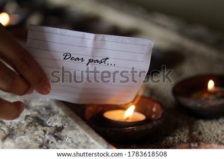 Hand holding a white note paper written - Dear past. Burning it on a burning candle in a ceramic bowl. Hope and new life concept. Royalty-Free Stock Photo #1783618508
