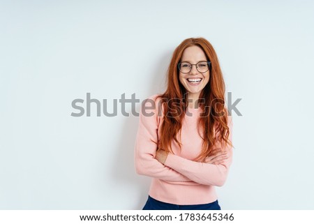 Happy vivacious young woman with a beaming smile standing with crossed arms against a white interior wall with copy space in an upper body portrait Royalty-Free Stock Photo #1783645346