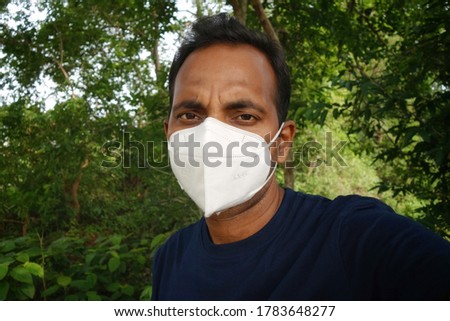Portrait of a young Indian man covering his face with a white color N95 anti-pollution mask while going outside. 