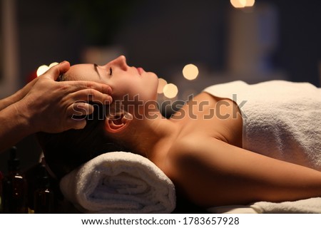 Woman lay on couch on her back with closed eyes and enjoy. Man make relaxing and therapeutic head massage at weight. Spa client has thrown her head back and rejuvenate. Wellness procedures in spa Royalty-Free Stock Photo #1783657928