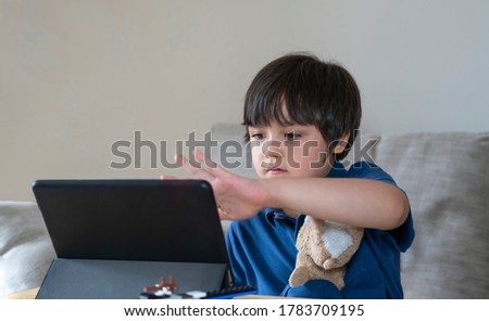 School Kid using tablet for his homework, Child looking at digital tablet with thinking face, Young boy watching cartoon on touch pad, new normal life stye with learning online, Distance education