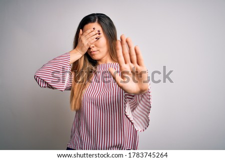 Young beautiful blonde woman with blue eyes wearing stiped t-shirt over white background covering eyes with hands and doing stop gesture with sad and fear expression. Embarrassed and negative concept.