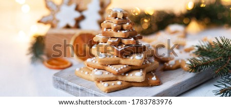 Fir tree made of delicious homemade gingerbread cookies decorated with icing. Rustic decor, christmas lights on. Festive mood, holiday atmosphere. Front view, closeup, white background. Banner