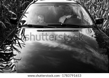 Black and white picture of a young Caucasian mom, beautiful dad and their cute child go to the village through a cornfield by car.