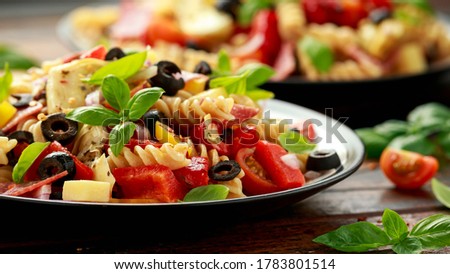 Antipasto salad with pasta, tomato, olives, red onion, bell pepper, salami, cheese, artichoke and basil.
