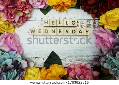 Hello Wednesday alphabet letter with colorful flowers border frame on wooden background