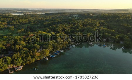 Aerial view of rural landscape with lush greenery and lake at dawn. The shoreline with boat docks. American Midwestern countryside scenery in the early sunny morning