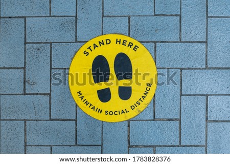 A circular Social distancing sign or sticker plastered on a brick floor near the entrance of a mall or shopping plaza.