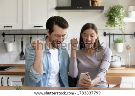 Excited young Caucasian husband and wife sit at kitchen feel euphoric win online lottery on smartphone app, overjoyed millennial couple  read unexpected news message or sale deal on cellphone Royalty-Free Stock Photo #1783837799