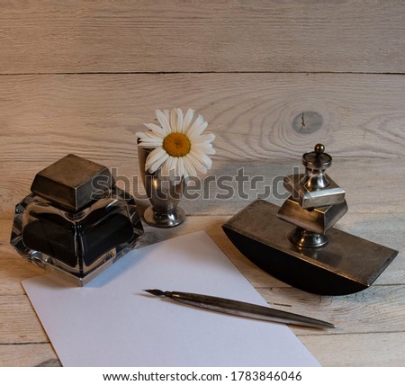 Still life from a silver writing set: inkwell, paperweight, pen, stamp and chamomile in a glass. Royalty-Free Stock Photo #1783846046