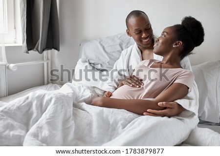 happy afroamerican married couple lie on bed, pregnant wife and handsome man expecting baby, full happy family. they smile, plan their common future