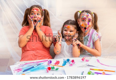 three children paint with paints.  girls smile happily and make fun.