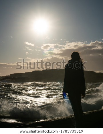 Beautiful silhouette of a girl posing in front of big waves crashing in over the rocky shore