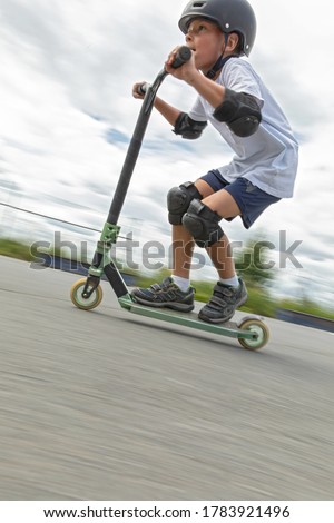 A cute little boy rides a scooter in a skatepark.  A young novice athlete spends free time in extreme sports. Motion photo, interchangeable motion blur.
