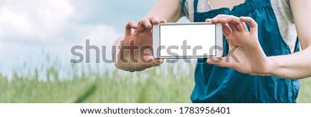 Banner, Mock up of a smartphone in the hands of a girl farmer, against the background of a green field.