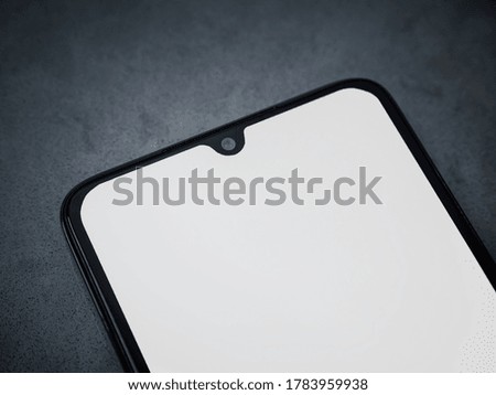 Black mobile smartphone mockup lies on the surface with a blank screen isolated on a dark marble stone background. Top view close up with selective focus and copy space, cut in the middle.