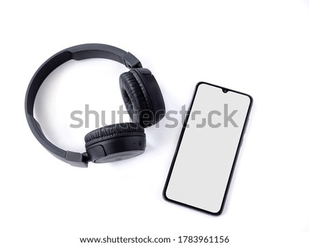Black wireless headphone and mobile smartphone with a blank screen mockup lay on the surface of a white background. Top view flat lay with copy space. Music concept.